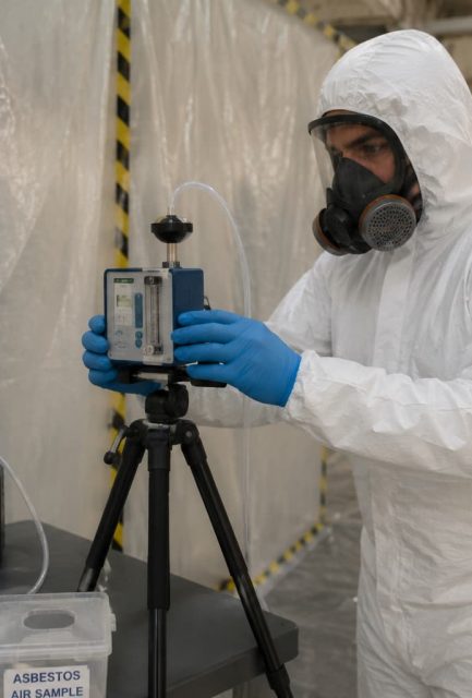 UKAS-accredited analyst operating air monitoring equipment during 4-stage clearance testing in a sealed Surrey enclosure.