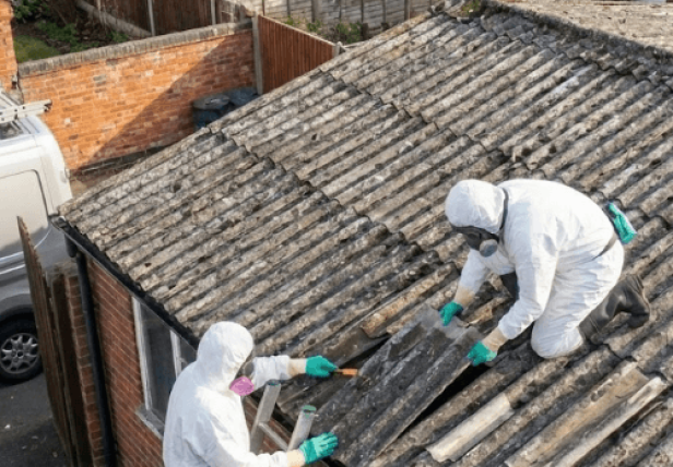 Two UKATA-trained operatives in full PPE removing degraded asbestos cement sheets from a Surrey garage roof.